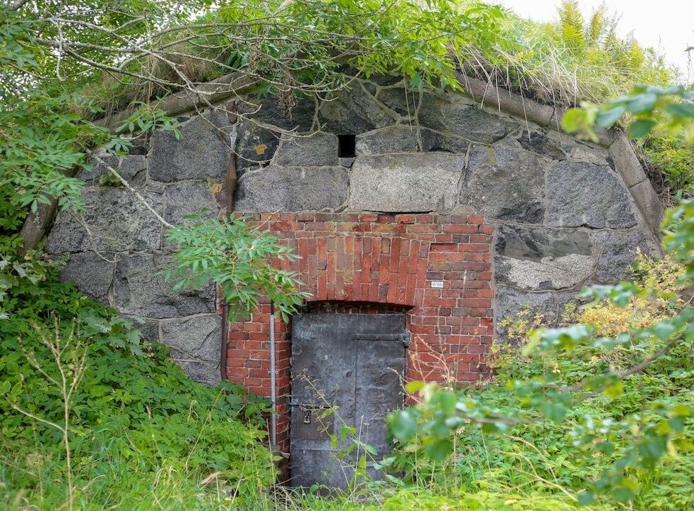 Gammal stenbyggnad med tegelinfattad järndörr i tät grönska
