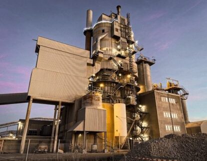 Industriell kalkugn med silor, rör och stora högar av kalksten