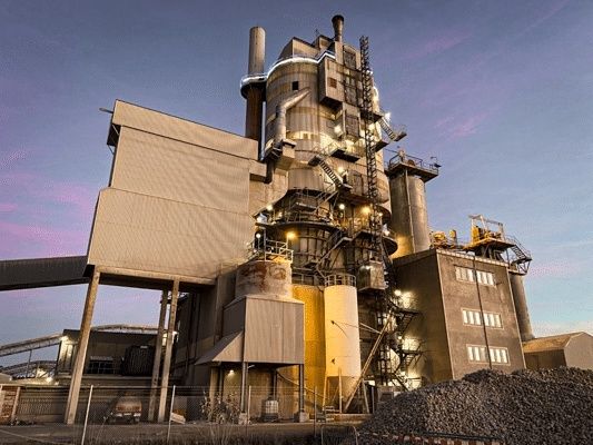 Industriell kalkugn med silor, rör och stora högar av kalksten